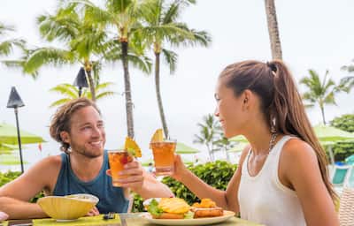 Man and woman drinking mai tai cocktails in a tropical location.