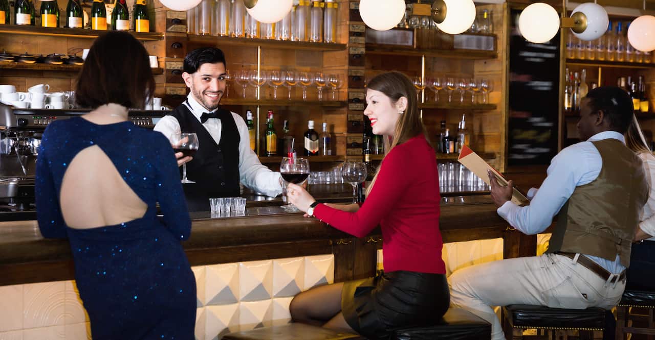 Vintage bar patrons receiving wine from a bartender.