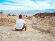 A young man sits in the middle of the desert at Zabriskie Point against the backdrop of the mountains, Death Valley
