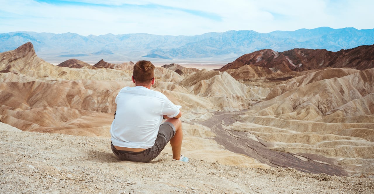 A young man sits in the middle of the desert at Zabriskie Point against the backdrop of the mountains, Death Valley