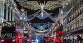Red double-decker buses pass under twinkling Christmas lights along the upscale shopping district of Regent Street in London.