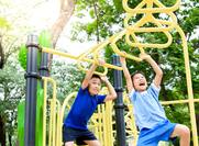 Two, young Asian boys playing on yellow monkey bars at a playground.