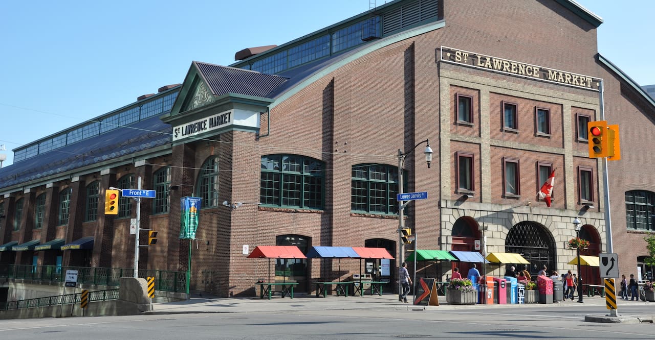 St. Lawrence Market - a large, industrial building that houses a public market in Toronto that has vendor tables with colorful tops outside.