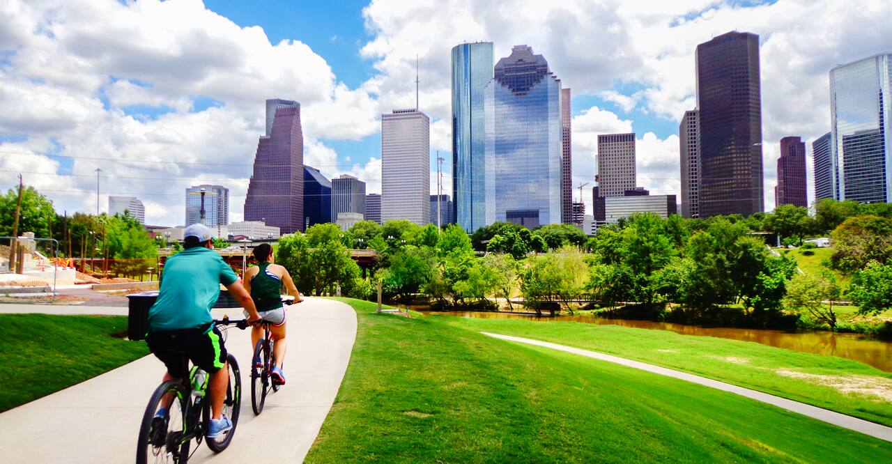 Two people riding bikes on paved trail in a Houston, Texas park.