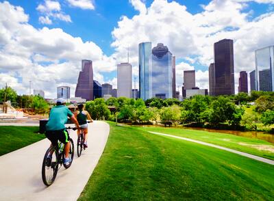 Two people riding bikes on paved trail in a Houston, Texas park.