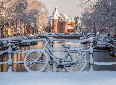 A snow-covered bike leaning against a railing in front of a canal in Amsterdam.
