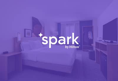 Spark by Hilton logo set on transparent purple over an image of a bedroom