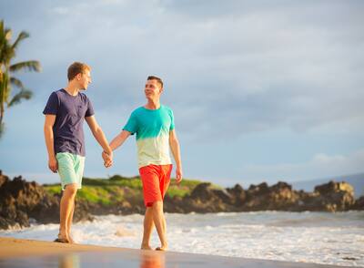 Gay couple holding hands while walking along a tropical beach.