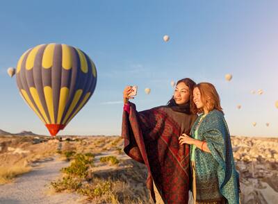 Two young Asian women posing for a photo in front of hot air balloons.