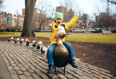 A boy riding a duck sculpture in a Boston park.