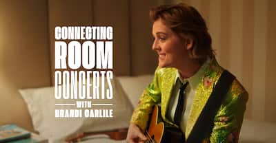 'Connecting Rooms Concerts with Brandi Carlile' text overlay on an image of Brandi Carlile sitting on a bed playing acoustic guitar