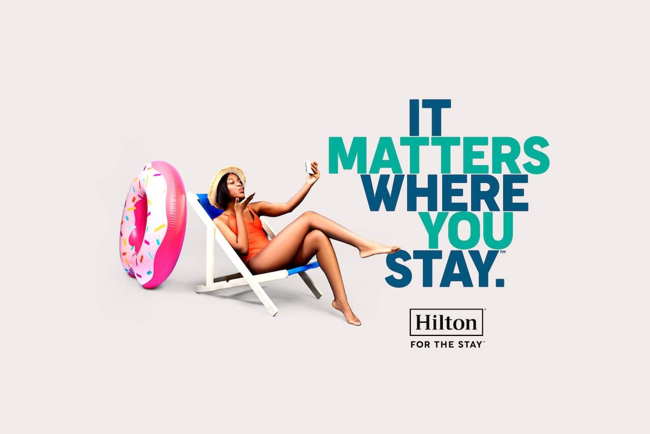 Woman taking selfie on deckchair, with text reading 'it matters where you stay. Hilton. For the Stay'