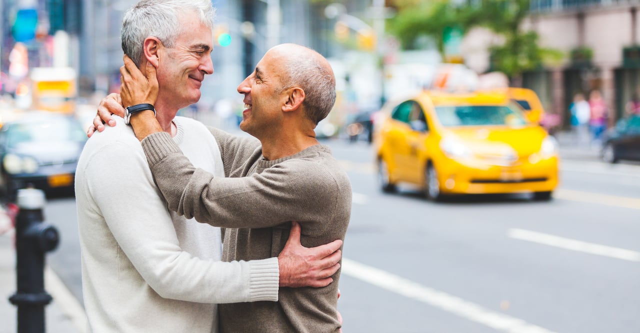 Two senior men hugging and cuddling each other next to a busy street in New York city.
