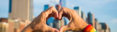 Mâini care poartă o bandă curcubee pentru transpirație cu mândrie de homosexualitate, simbolizând inima în fața orizontului orașului.