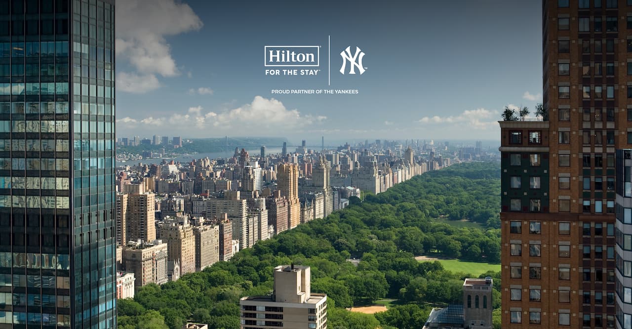  Ariel view of central park with the manhattan skyline surrounding it. The 'Hilton: For The Stay' and New York Yankees logo is displayed over the image.