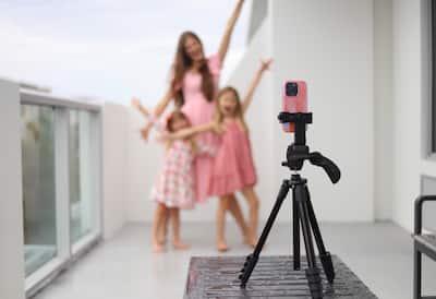Three people in dresses pose for a phone camera positioned on a tripod