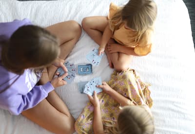 Three girls sit on bed playing cards together