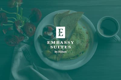 A breakfast plate with the Embassy Suites Hotels by Hilton logo layered over the top