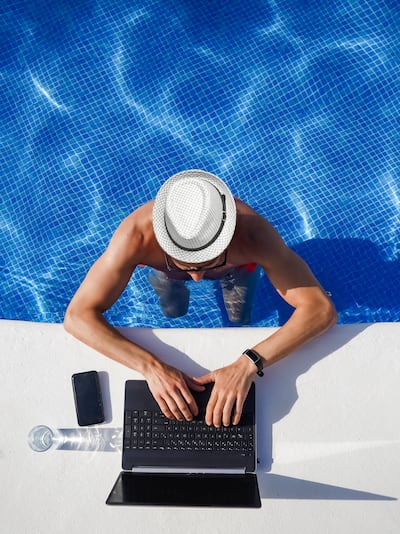 Man in hat stands in pool and works on laptop