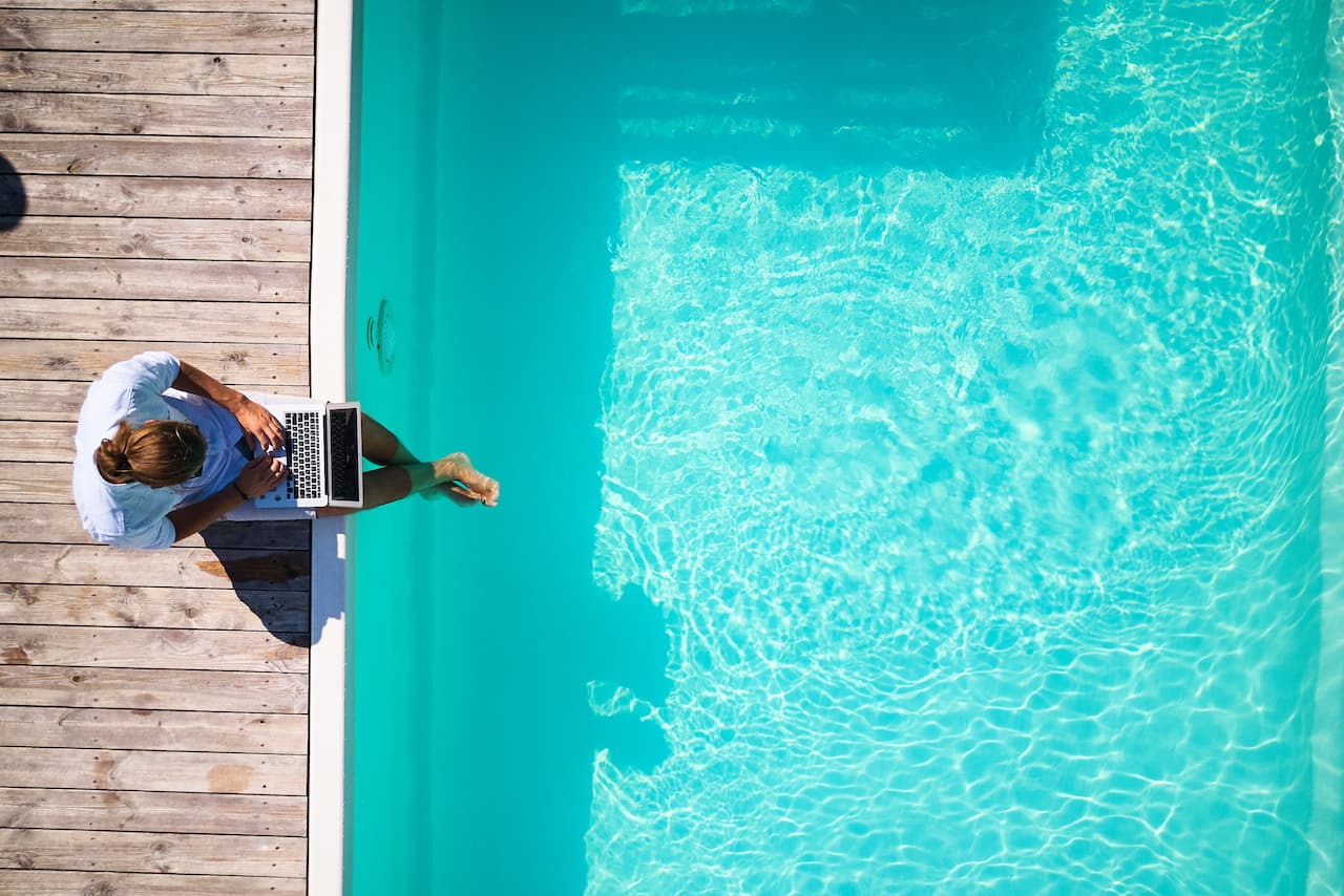 Yüzme havuzunda feet dizüstü bilgisayara bakan adam