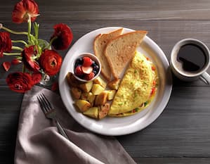 Breakfast plate of pepper and cheese omelet with toast, fruit, potato pieces and a cup of coffee