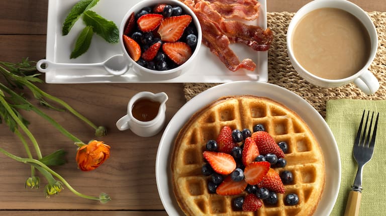 Waffle Topped with Strawberries and Blueberries and a side of Bacon, Fruit and Coffee