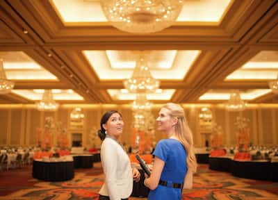 Two women standing in a banquet room looking surprised. 