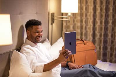 Business Man Sitting on Guest Room Bed and Looking at Tablet