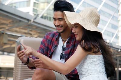 Smiling man and woman in a straw hat standing outside looking at mobile device intently.