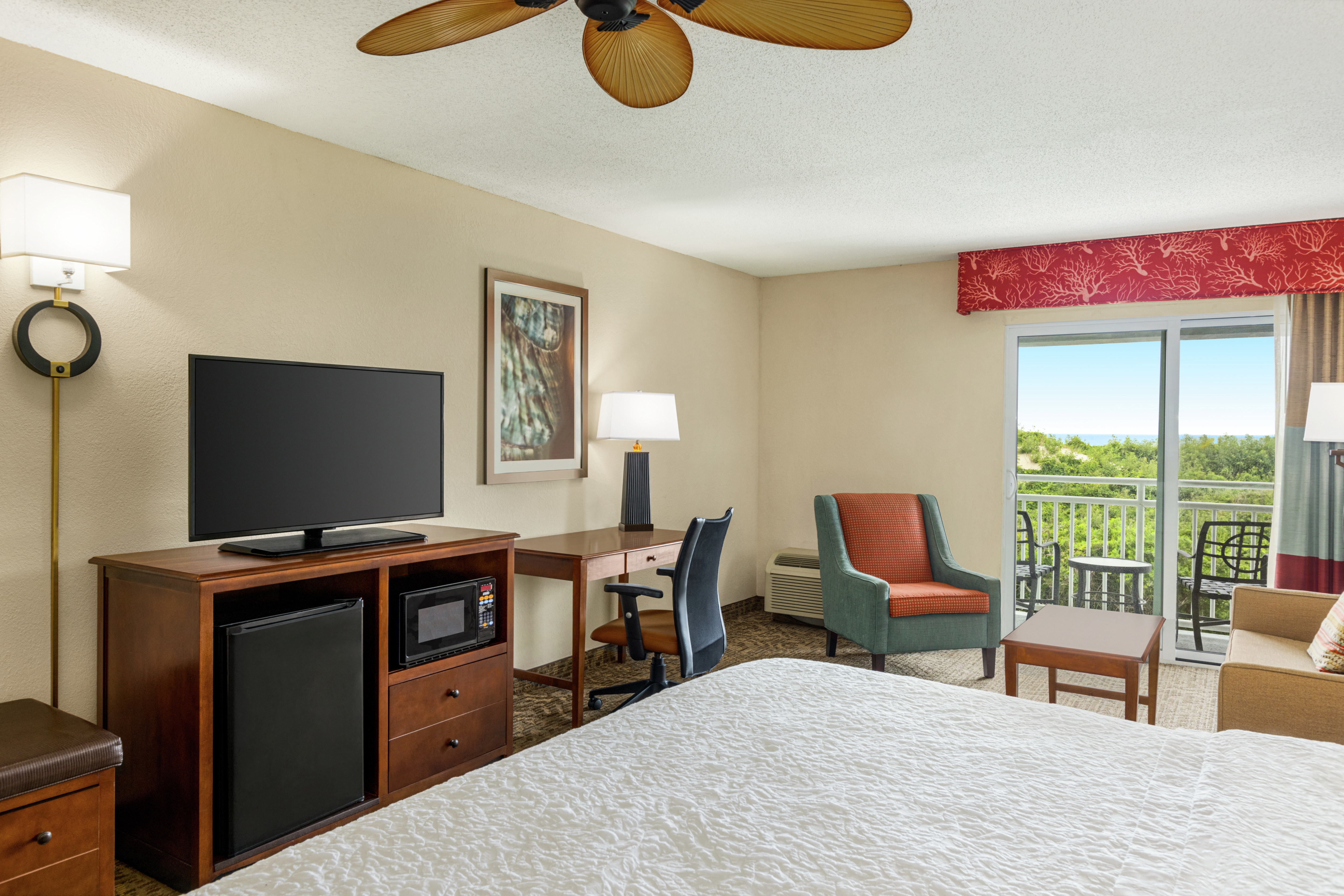 Spacious guestroom featuring comfortable bed, TV, work desk, sofa, and private balcony.