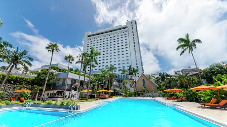 プールとプールサイドに配されたラウンジチェア&パラソル、ホテルの建物