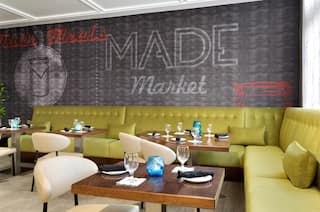 Wall Mural Behind Green Sofa Seating, Tables With Place Settings, and Chairs in Restaurant