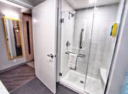 Door Opening Into Guest Bathroom with Glass Shower with Seating, Handrail and Towel
