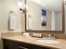 Wall Art and Shower Curtain Reflected in Vanity Mirror, Sink, Fresh Towels, and Amenities in Standard Bathroom
