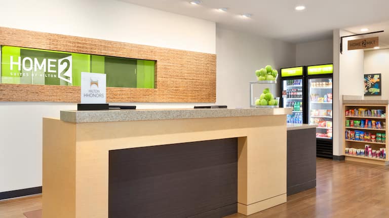 Hotel Signage Behind Front Desk With Green Apples on the Counter and View of the Snack Shop
