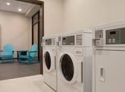 Open Doorway to View of Two Blue Chairs, Spin2 Cycle Laundry Room With Coin Operated Washing and Drying Machines