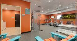 Two Blue Chairs Facing Door Opening to Laundry Facility, Large Room With Exercise Equipment, Large Spin2 Cycle Sign by Window, and Towel Station in Fitness Center