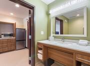 Open Doorway With View of Kitchen, Brightly Lit Vanity Mirror, Sink, Fresh Towels, and Amenities in Accessible Bathroom