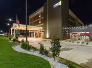  Angled View of Illuminated Exterior Entrance, Driveway, Flagpole, Landscaping, Signage, and Patio at Night
