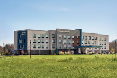 Welcoming Hampton Inn hotel exterior featuring lush landscaping and blue sky.