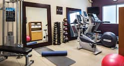 Fitness Room With Red Exercise Ball, Weight Machine, Bench, Large Mirrors, Exercise Mats, Free Weights, Weight Balls,  Cardio Equipment, TV, and Wall Clock