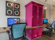 Red Storage Cabinet Between Two Computers on Long Desk, Wall Art, and Two Ergonomic Chairs in Business Center