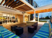 Illuminated Outdoor Patio Lounge Area With Pavilion, Four Square Tables, and Striped Sofas by Square Fire Pit at Dusk