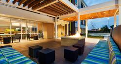 Illuminated Outdoor Patio Lounge Area With Pavilion, Four Square Tables, and Striped Sofas by Square Fire Pit at Dusk