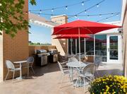 Chairs, Two Grills, Tables With Red Umbrellas Under String Lights on Outdoor Patio on a Sunny Day