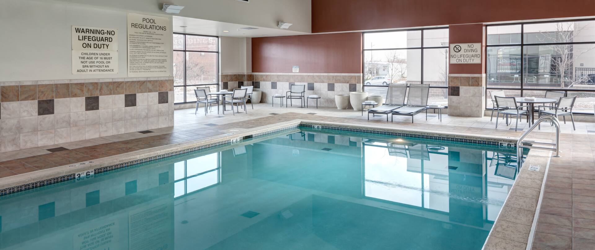Indoor Pool With Chair and Table Seating, Loungers, and Windows With Outside Views