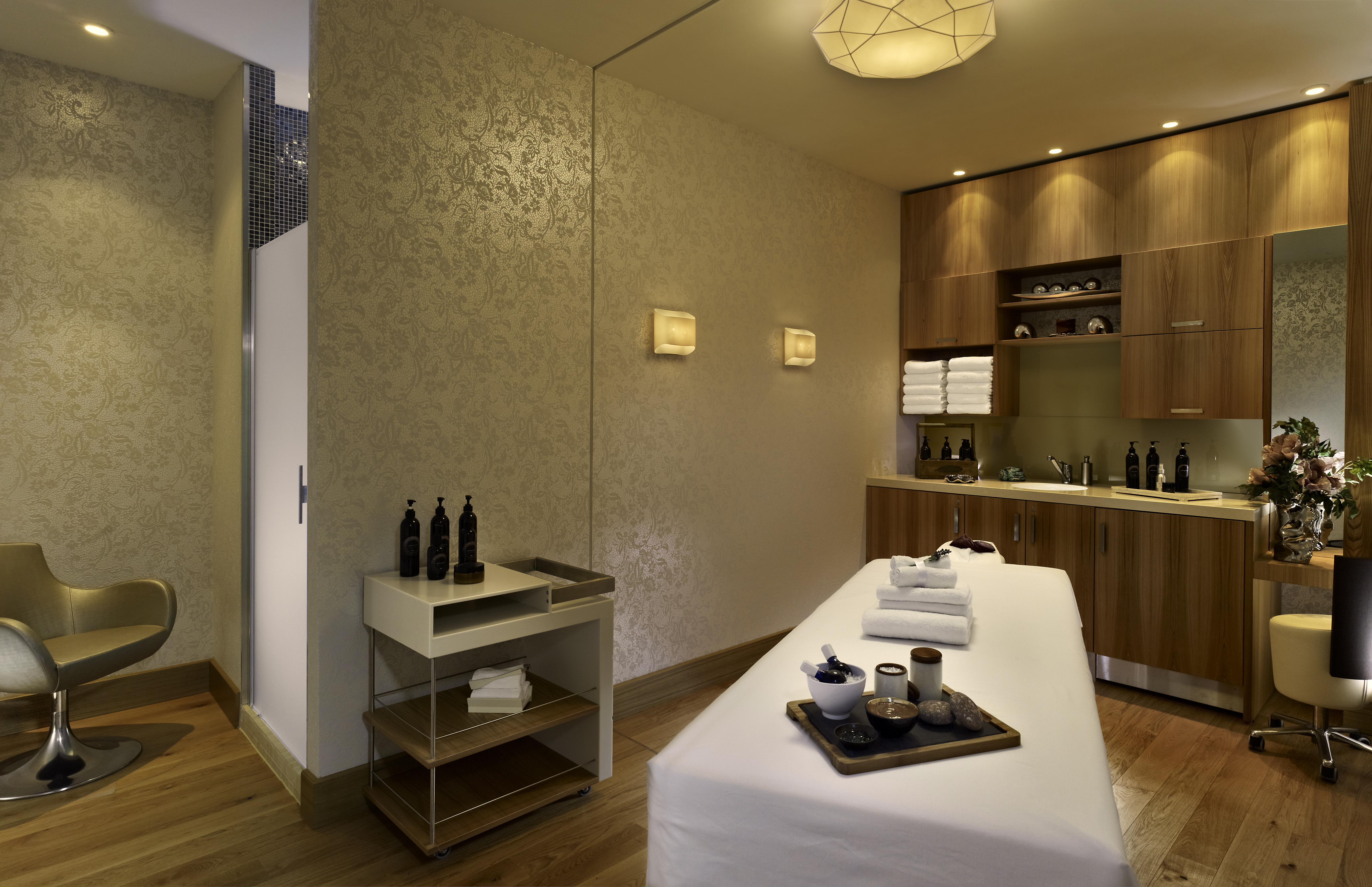 Spa Treatment Room With Chairs, Massage Table, Sinks and Fresh Towels in Wood Cabinet