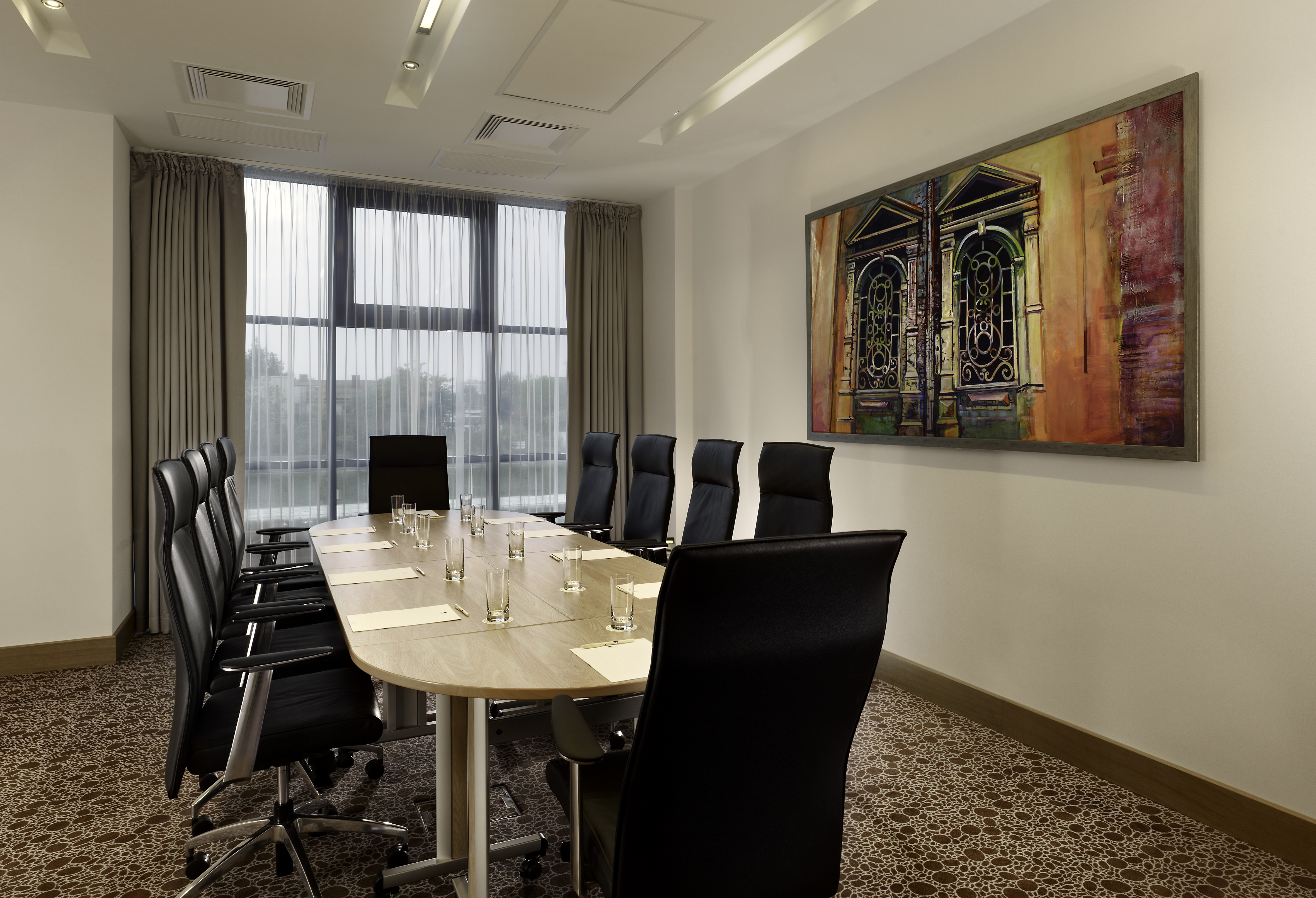 Window With Sheer Drapes, Wall Art, and Seating for 10 at Boardroom Table With Drinking Glasses, and Notepads in Augustia Boardroom