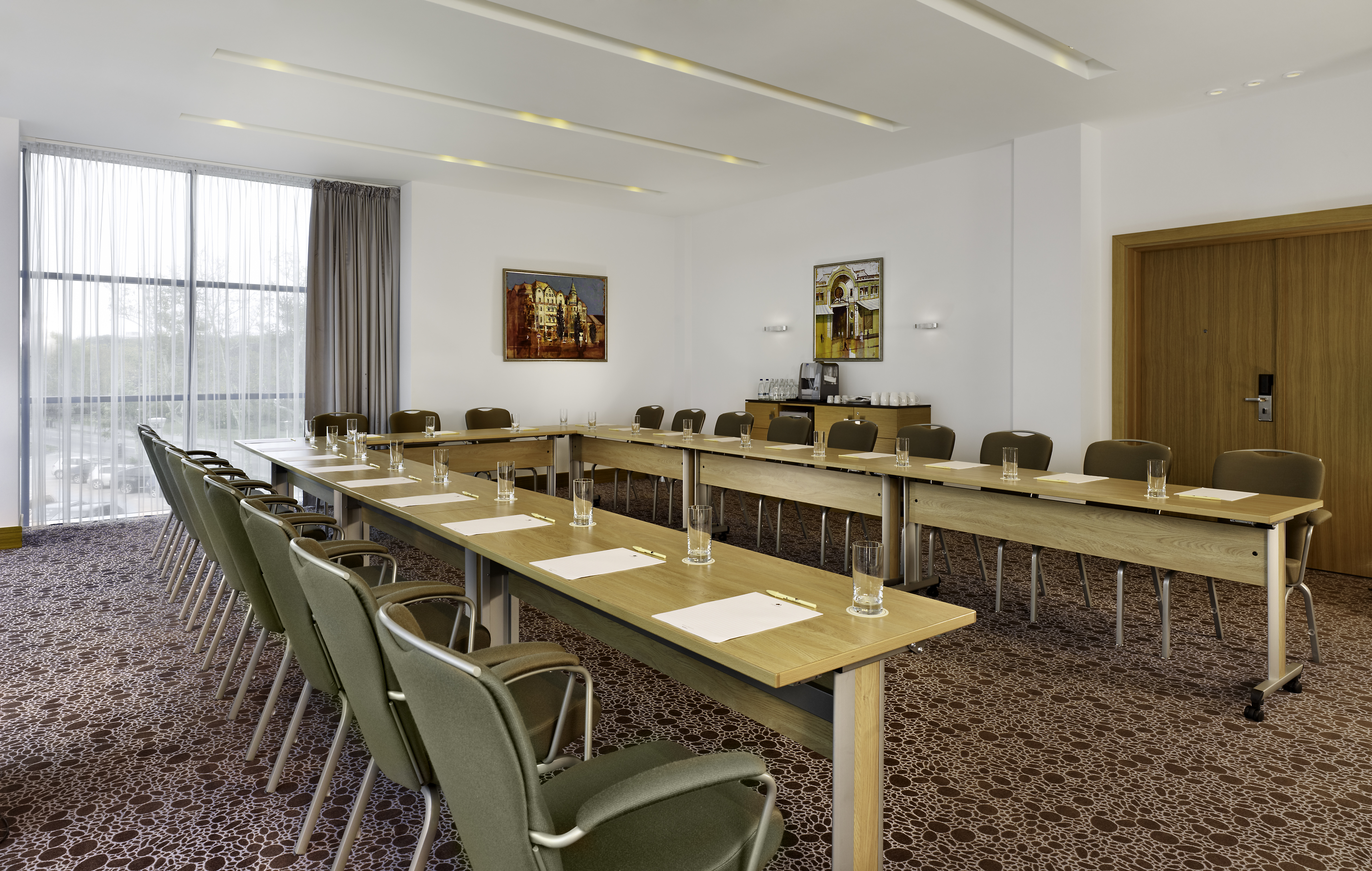 Donaris Meeting Room With Drinking Glasses, Notepads, Pens, and Seating for 21 at U-Shaped Table, Window With Sheer Drapes, Wall Art, Beverage Station and Entry Door