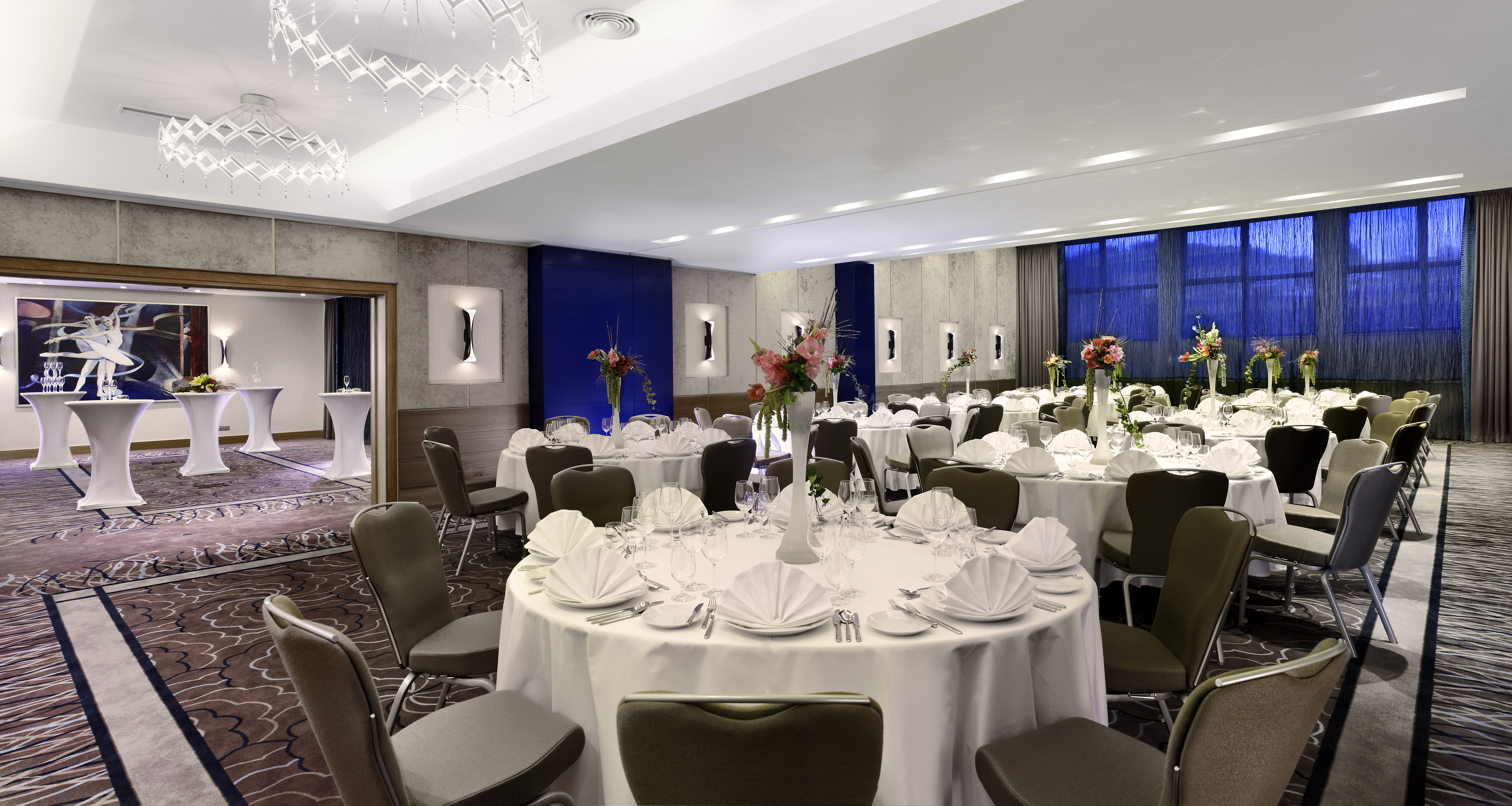 Varadinum Ballroom With With Place Settings, Flowers and White Linens on Round Tables, Chairs, Windows With Sheer Drapes, and View of Cocktail Tables and Wall Art in Breakout Room